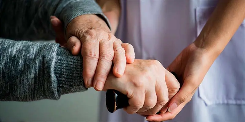 Manos de una enfermera joven apoyando y sujetando las manos de una persona mayor