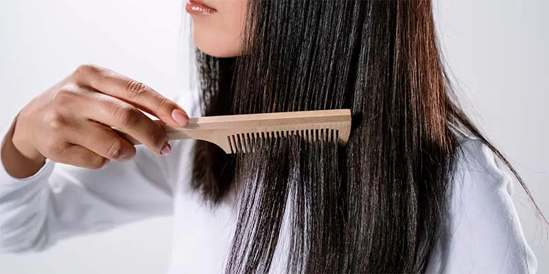 Mujer peinando su cabello con un peine de madera