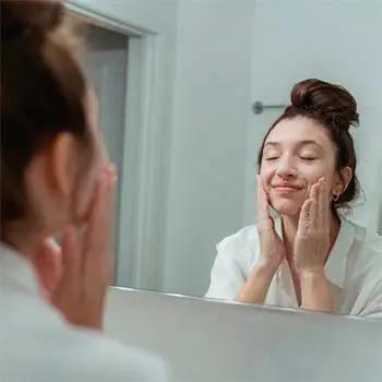 Mujer llevando a cabo su rutina de cuidado de la piel y lavando su cara frente al espejo