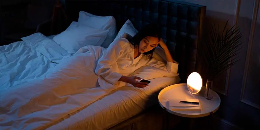Mujer que sufre de insomnio utilizando su móvil de noche intentando dormir